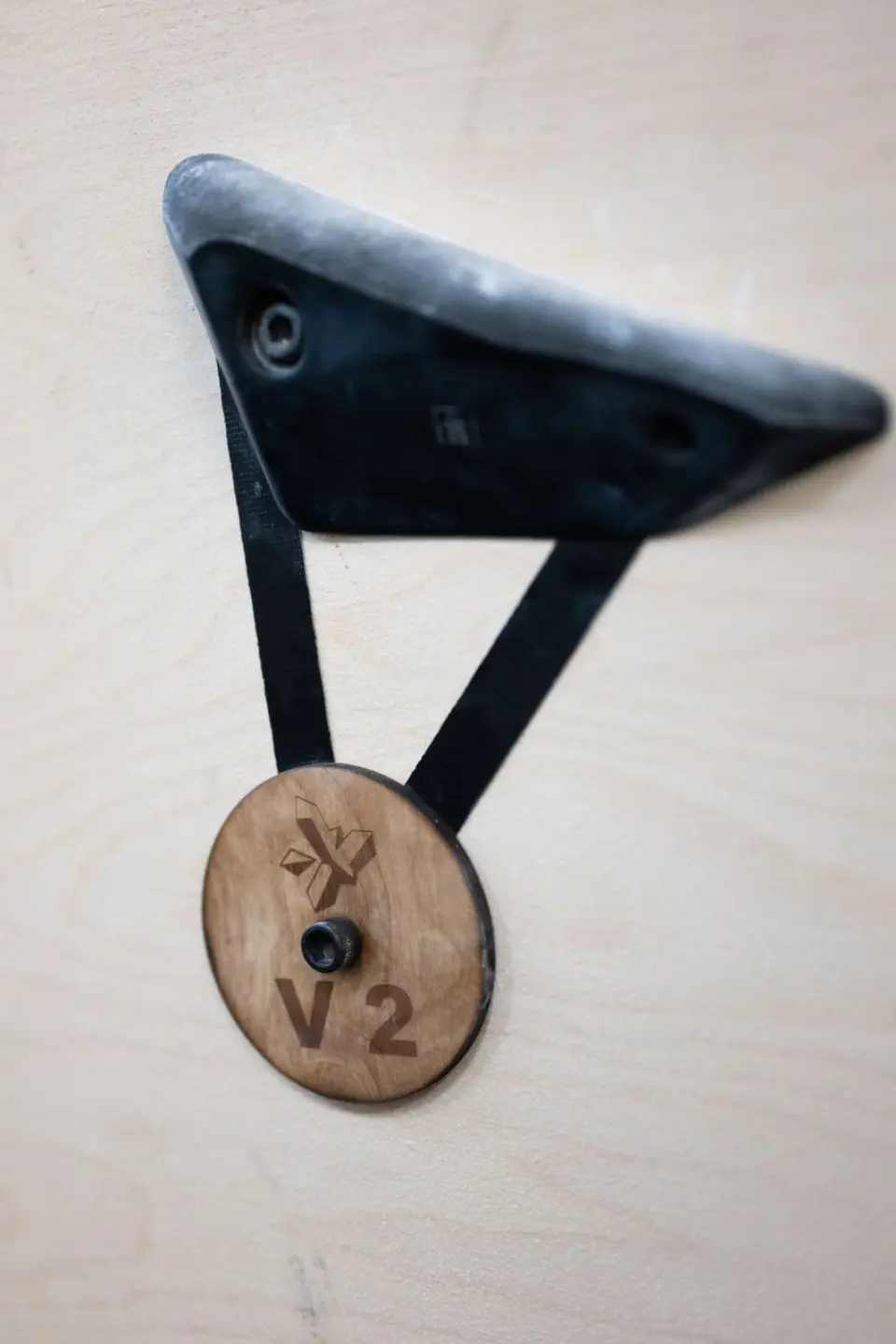 Black climbing hold with a wooden V2 grade tag on a plywood wall