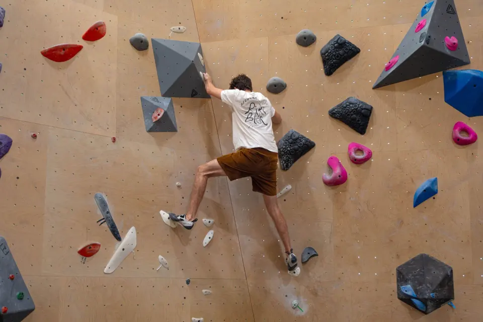 Climber stepping up between grey and black volumes on a plywood bouldering wall