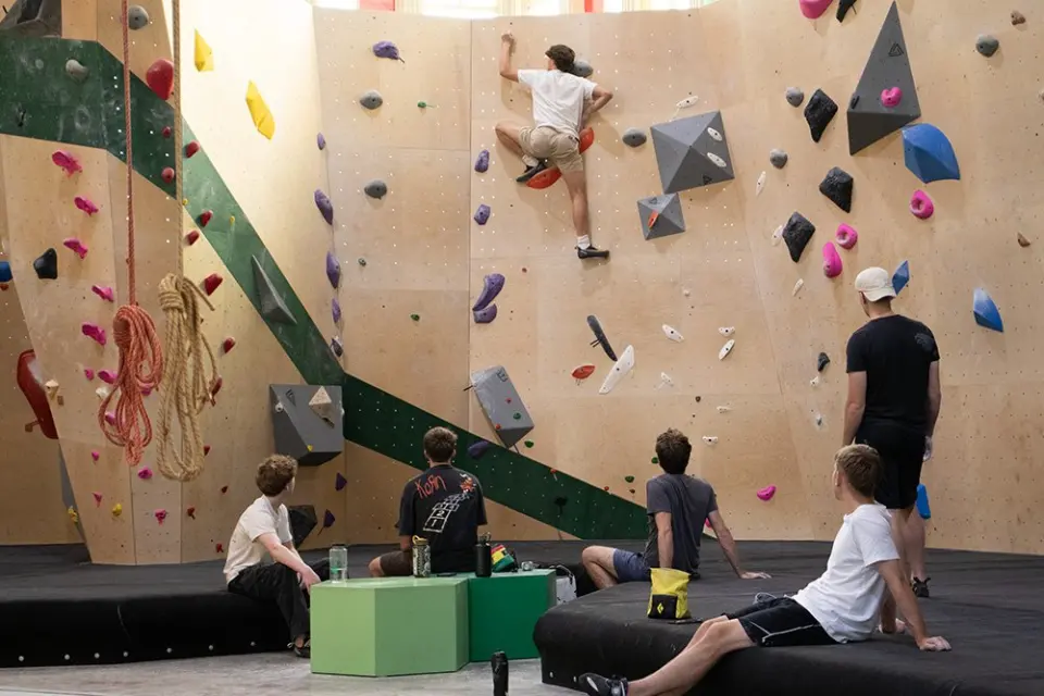 Climbers resting on the mats while another climbs the bouldering wall