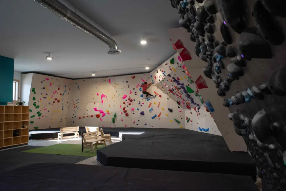 Bouldering room with a climber on the far wall, thick black matting, benches and the Grasshopper board on the right