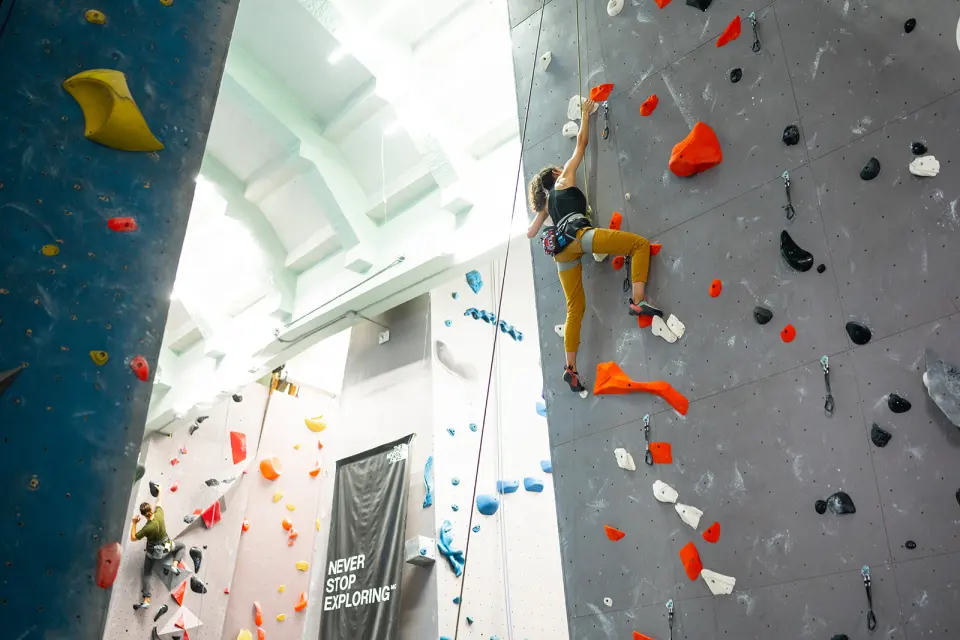 Climber on a tall grey top-rope wall beneath the church's pale vaulted ceiling