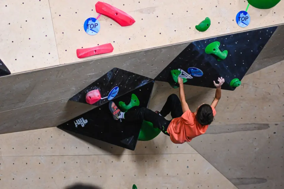 Climber reaching between black volumes on a steep plywood bouldering wall