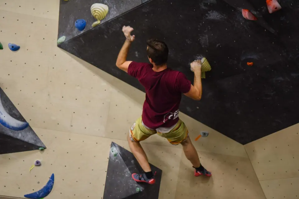 Climber pulling onto a large black volume on a plywood bouldering wall