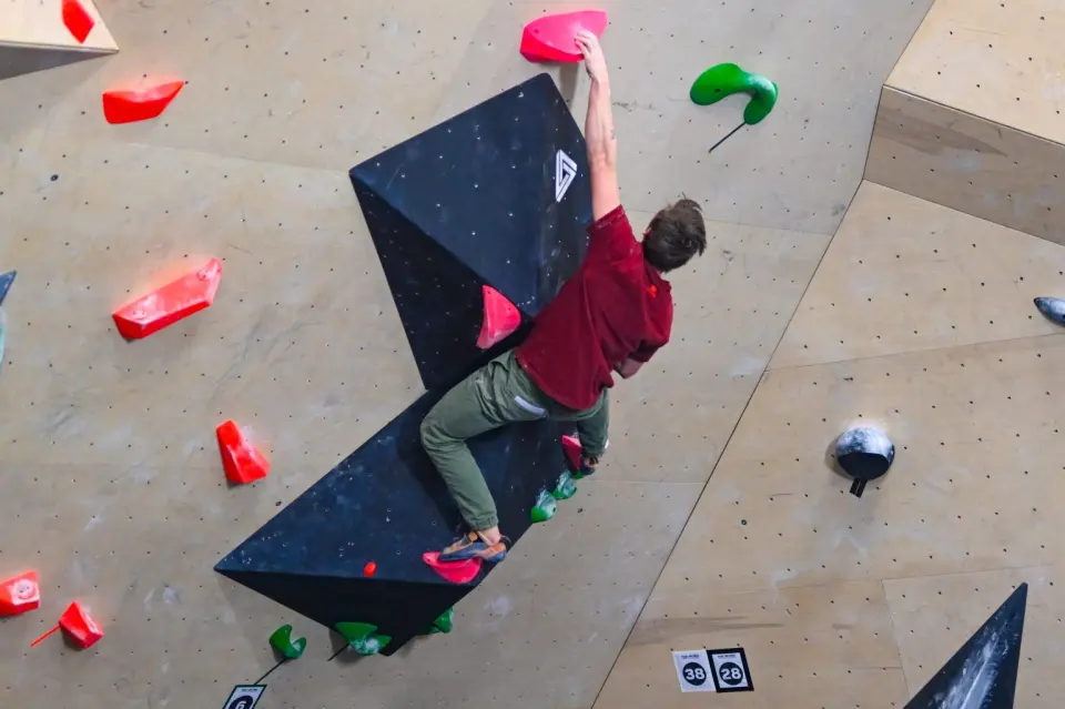 Climber on a dark triangular volume surrounded by red and green holds