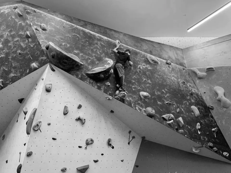 Black-and-white view of a young climber on an angular overhanging bouldering wall with large volumes