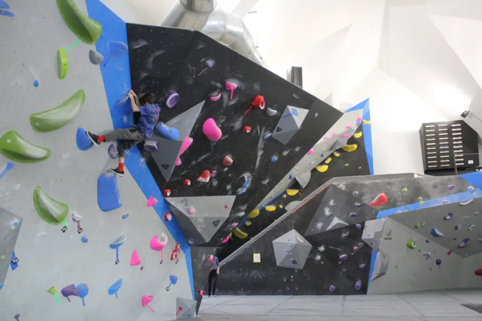 Black, grey and blue bouldering walls with angular volumes under a white vaulted ceiling