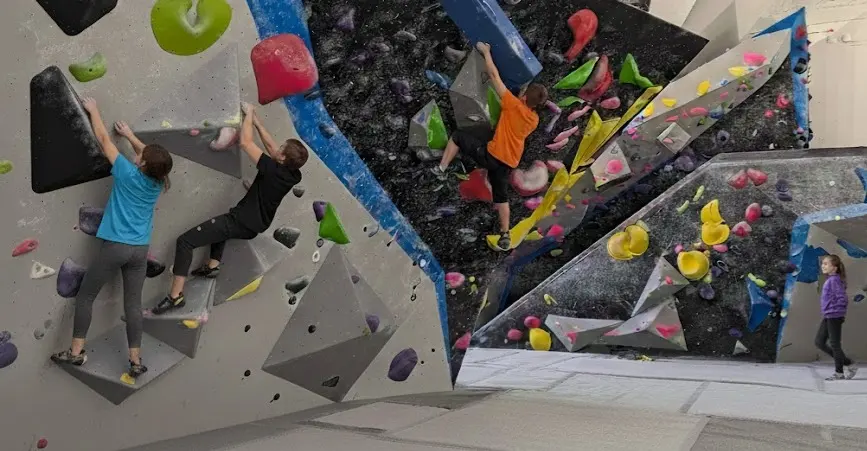 Young climbers on grey and black bouldering walls with yellow and pink holds