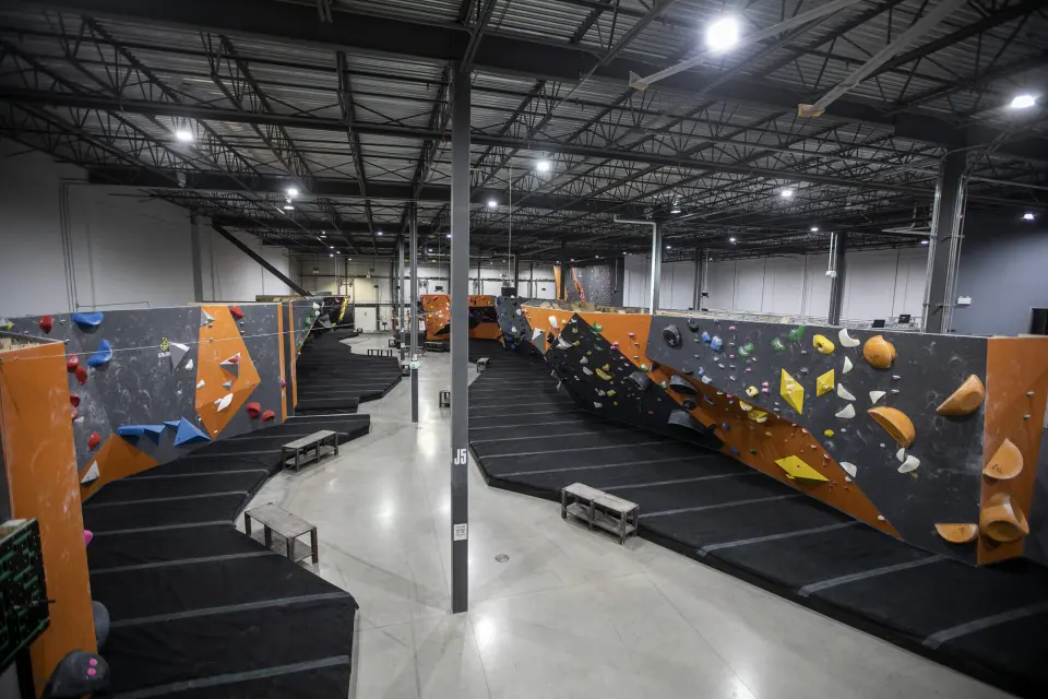 Rows of orange and grey bouldering walls above black matting in the empty hall at Altitude Gym Kanata