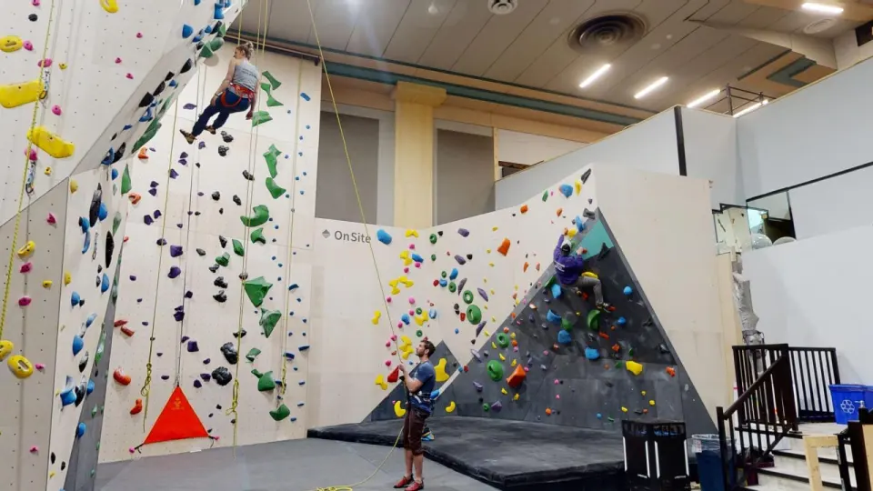 Climbers on a tall roped wall and an angled bouldering wall in a converted cinema hall