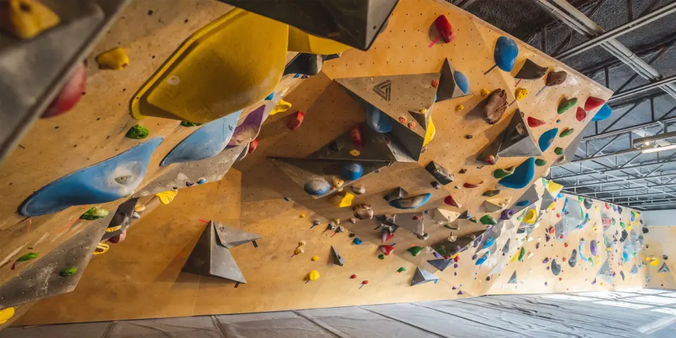 Long wooden bouldering wall with grey volumes and colourful holds above grey matting