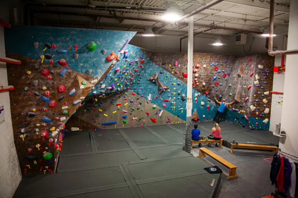 Bouldering room with teal and brown walls, a steep prow and benches on the matting