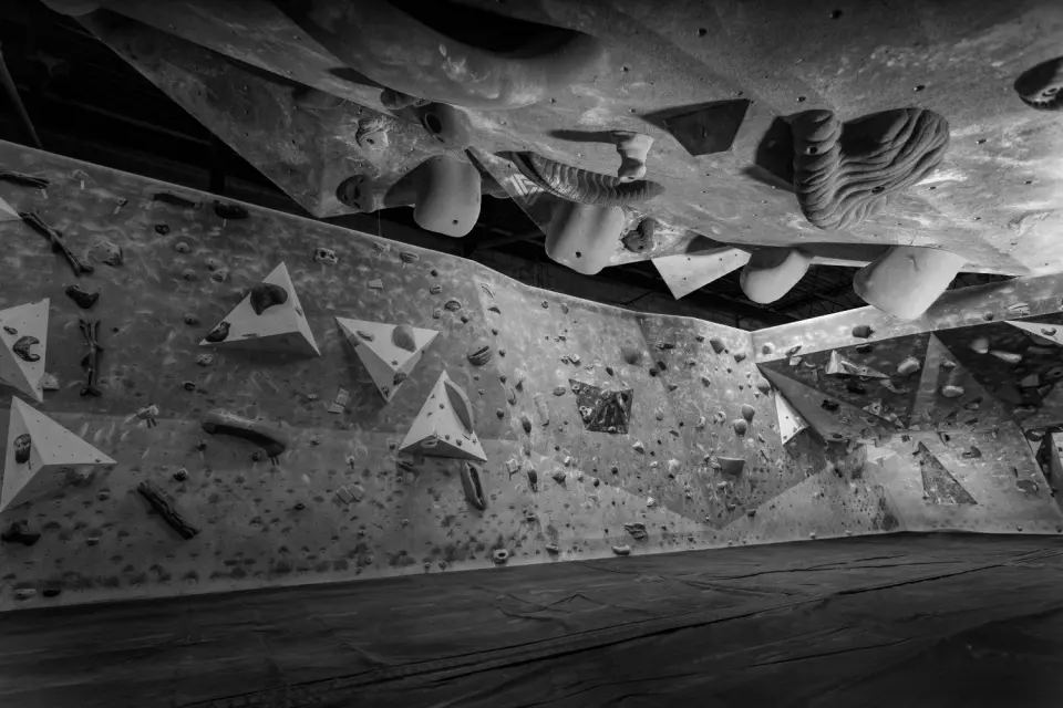 Black-and-white view of long bouldering walls under an overhanging roof with large volumes
