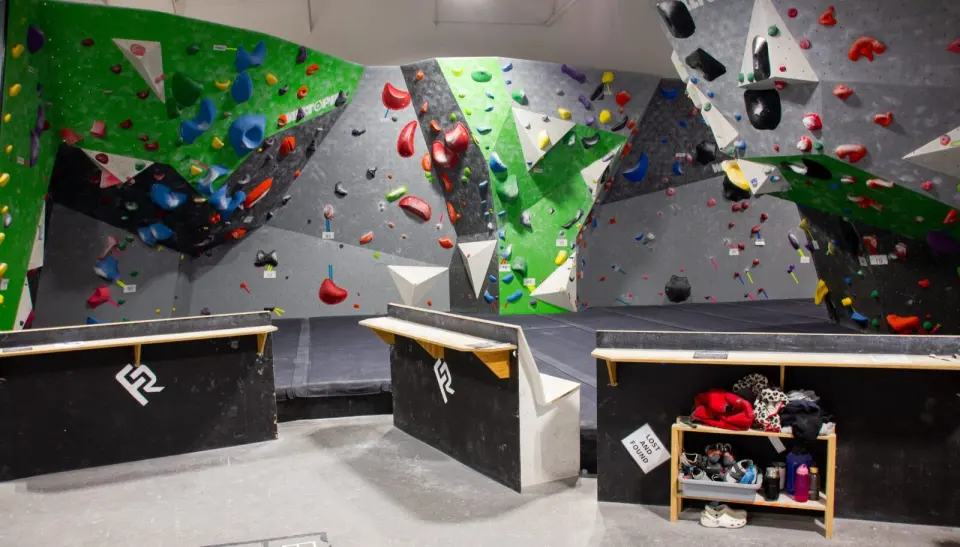 Green and grey bouldering walls with colourful holds above thick mats and benches