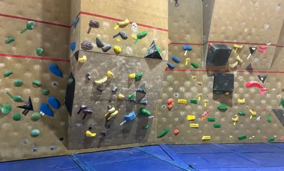 Bouldering wall with red height-limit lines and blue crash pads