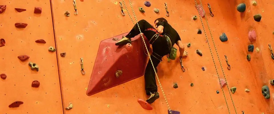 Climber stepping onto a large red volume on the orange lead wall, with quickdraws alongside