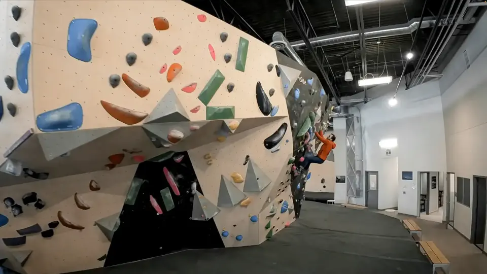 Big cream bouldering wall with blue and grey volumes above grey matting at Hive Winnipeg