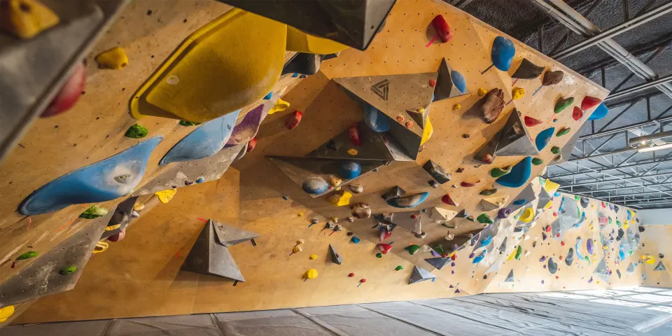 Long wooden bouldering wall with blue and grey volumes above grey mats at Seven Bays Bouldering on Gottingen Street, Halifax