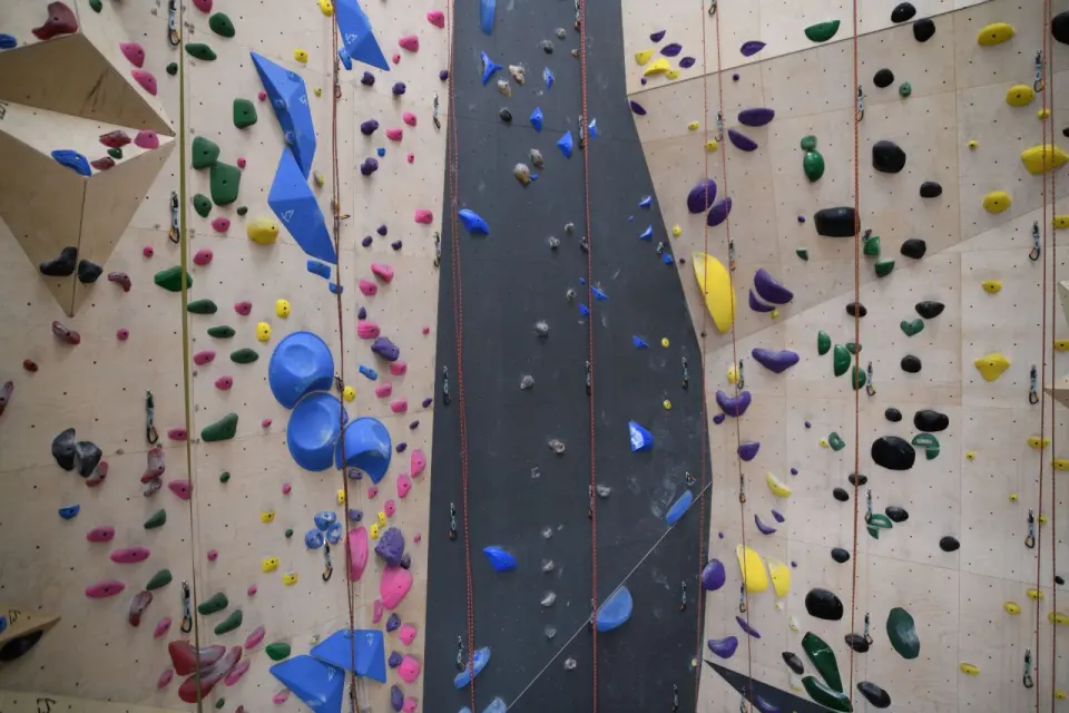 Tall roped wall with quickdraws, hanging ropes and a dark central lane of holds