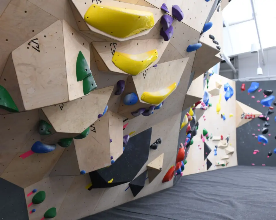 Plywood bouldering wall with angular volumes and yellow holds above thick matting