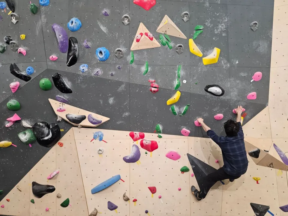Climber pulling on pink holds on a grey and plywood bouldering wall