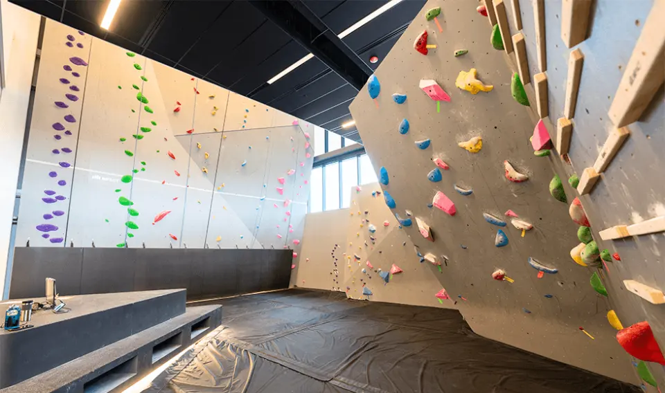 Bouldering area with padded flooring, with the top-rope wall behind