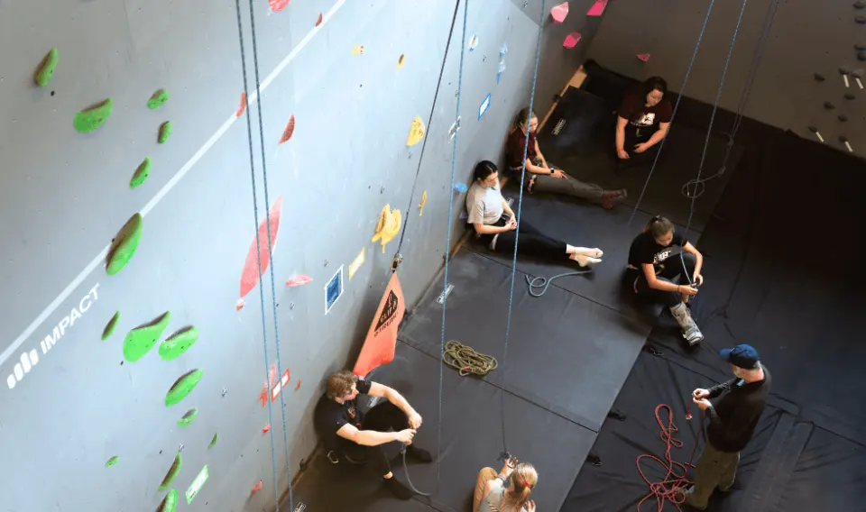Group sitting on the mats at the foot of the roped wall