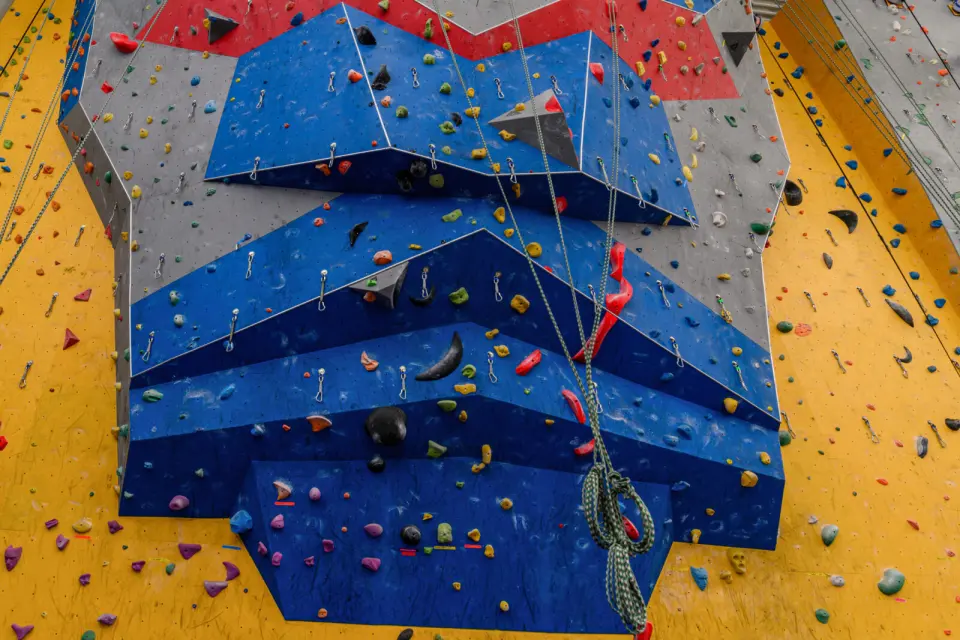 Tall roped climbing wall with blue and grey overhanging panels and ropes hanging down