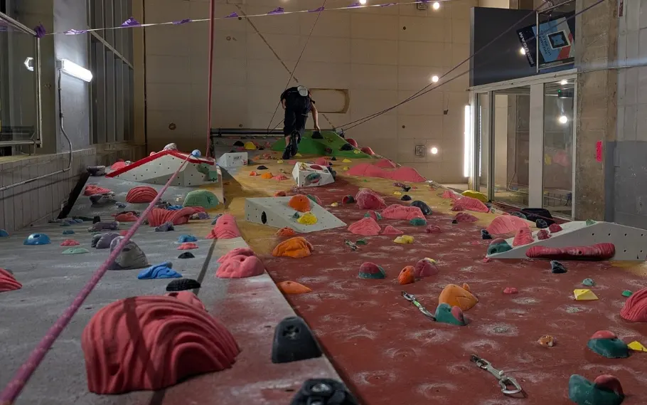 Looking up the climbing wall from its base, with holds, volumes and a climber near the top
