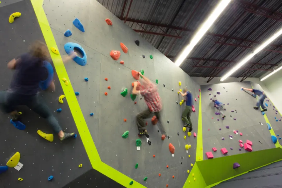 Climbers on grey bouldering walls with lime-green edges under a warehouse roof