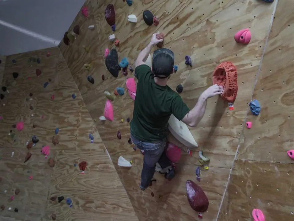 Climber reaching for holds on an angled plywood bouldering wall