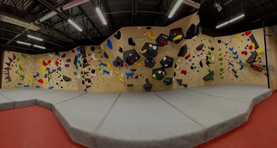 Wide bouldering wall with black volumes and colourful holds above thick grey mats at The Cove, St. John's