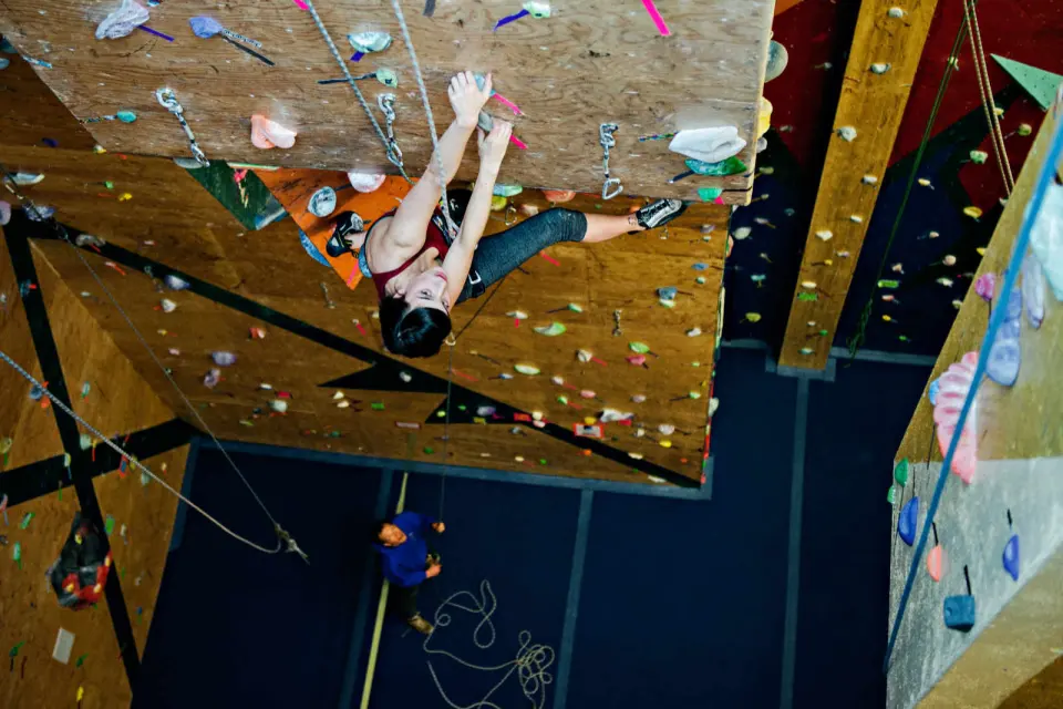 Climber on the steep overhanging wall, seen from below, with ropes hanging from the top
