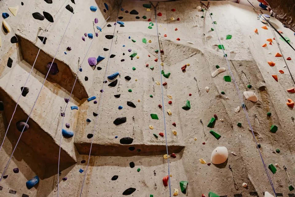 Tall textured top-rope wall with overhanging bulges, coloured holds and hanging ropes