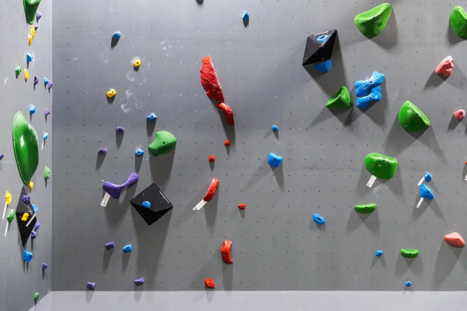 Grey bouldering wall set with coloured holds and black volumes