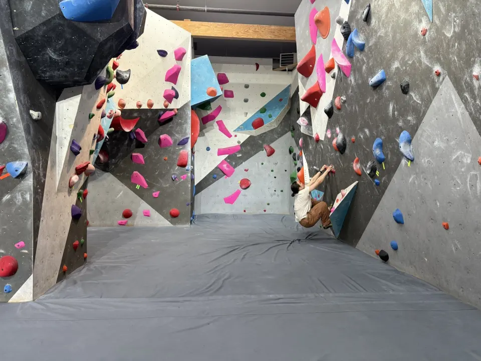 Climber on a steep grey wall in a bouldering corridor lined with pink, red and blue holds