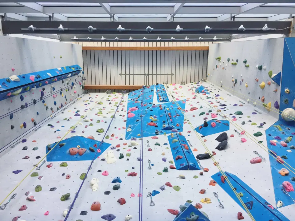 Looking up the tall roped wall with blue volumes and top ropes under a glass roof