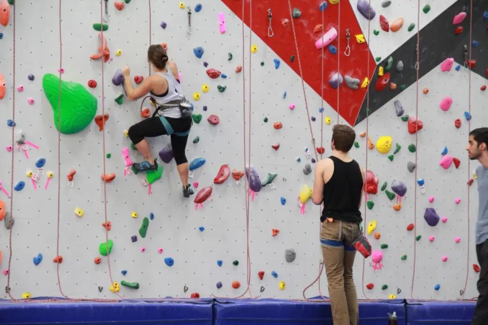 Climber on a top rope with a belayer below, above blue floor mats