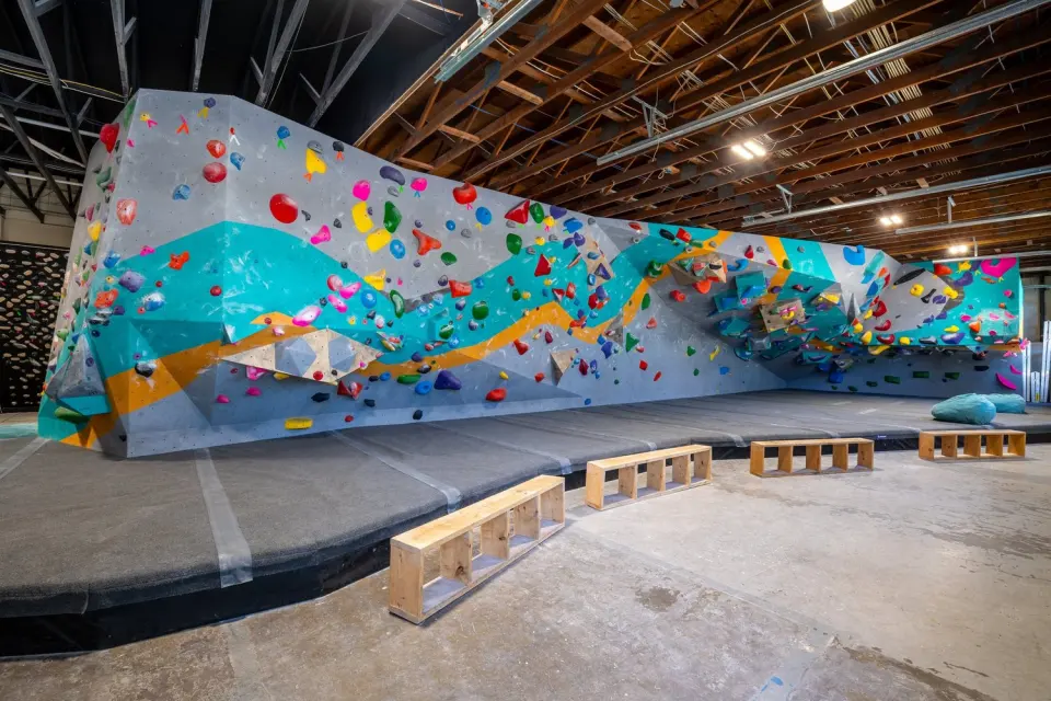 Long bouldering wall painted with teal and orange waves above thick black matting