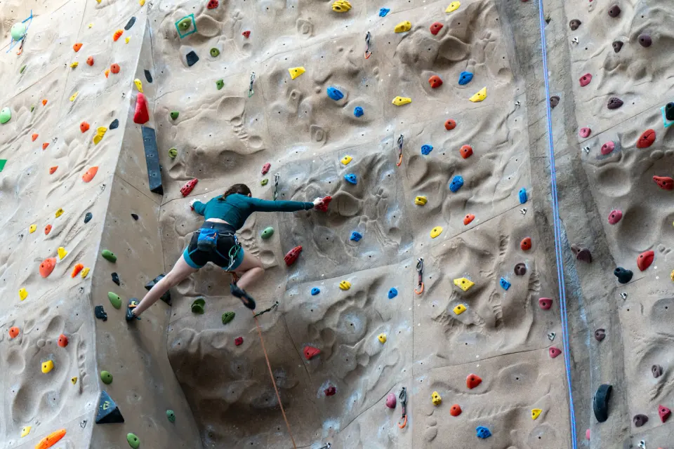 Lead climber on a tall sculpted climbing wall with colourful holds and quickdraws