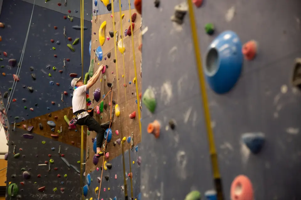 Climber clipping a rope on a tall blue and brown wall hung with auto-belay straps