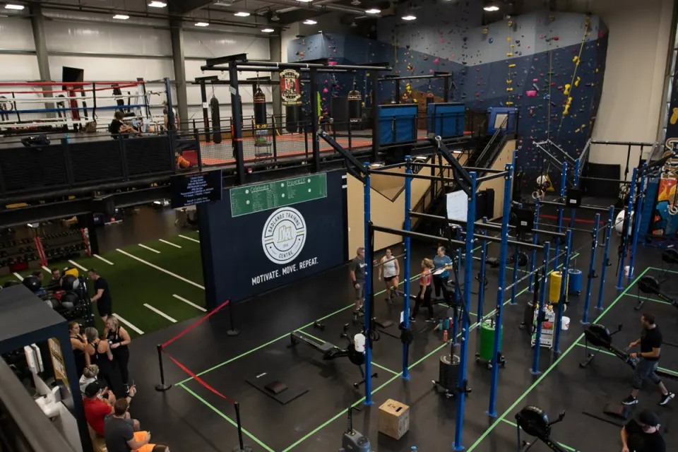 Fitness floor with a training rig and boxing ring, and the climbing wall rising at the back
