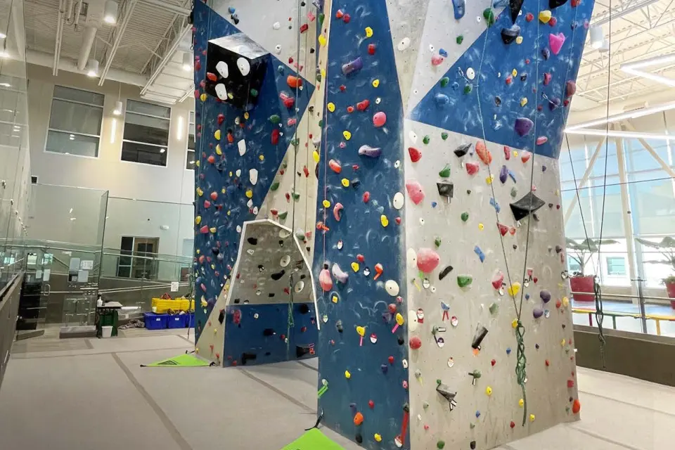 Blue and grey multi-faced climbing towers with top ropes, inside a bright sports hall