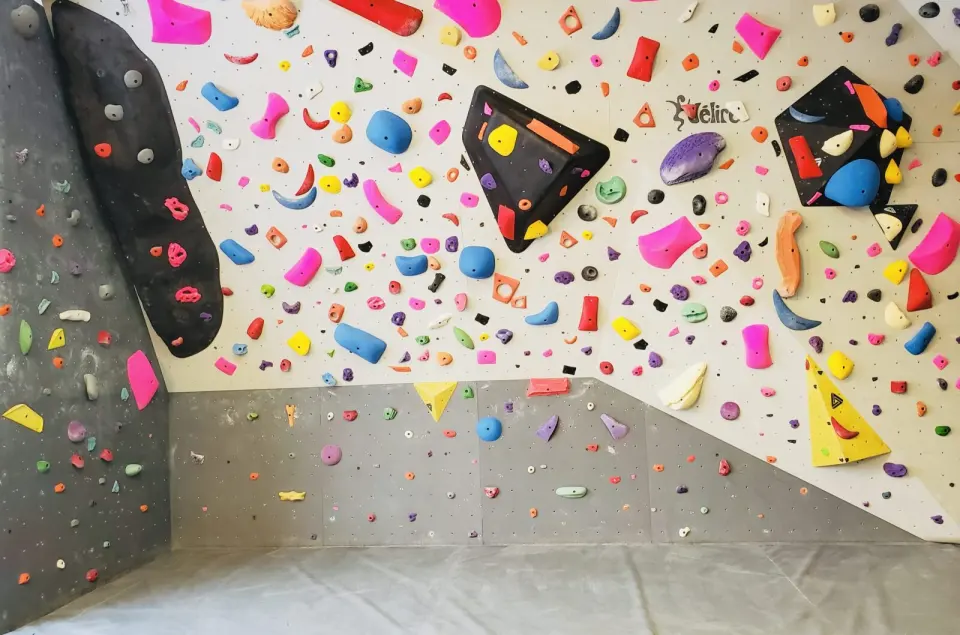 Spray wall densely covered in colourful holds and volumes above grey crash mats