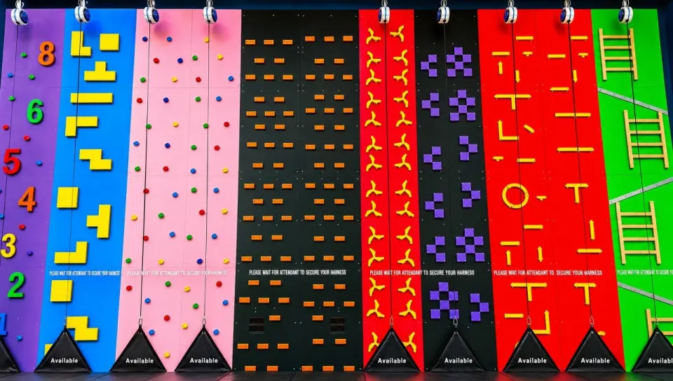 Row of colourful auto-belay climbing lanes with shaped holds and ladders