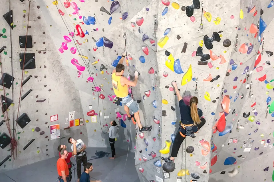 Lead climbers on the tall grey walls of the main hall, with belayers below