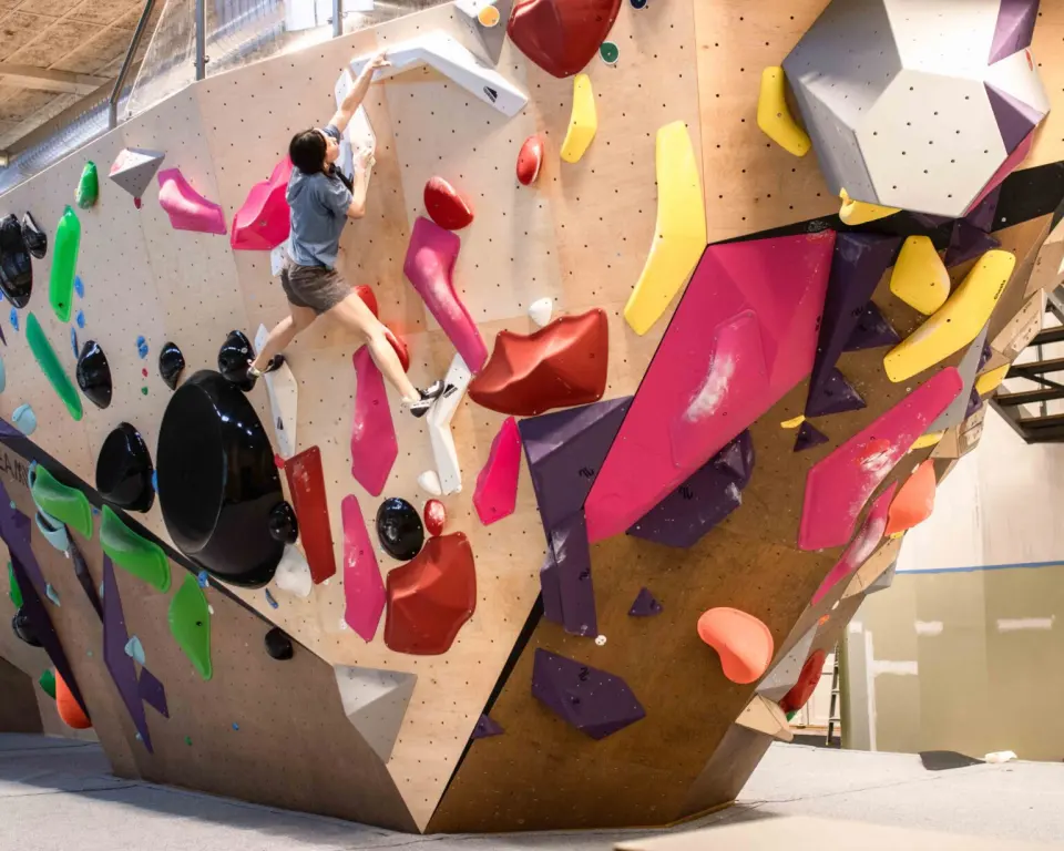 Climber on a large wooden bouldering island covered in colourful holds and volumes