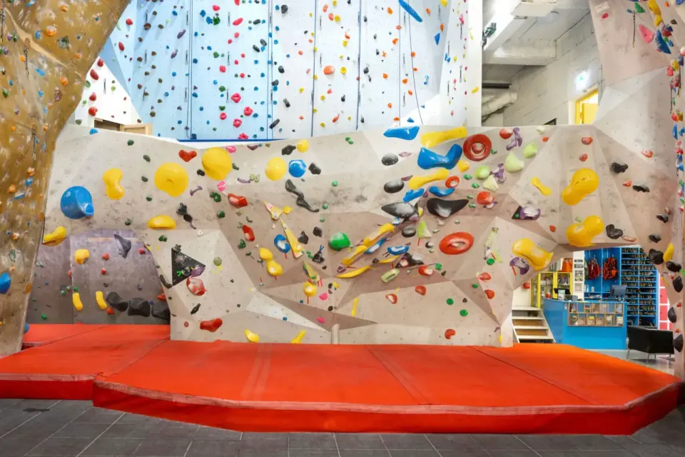 Bouldering wall with red matting in the main hall, with the tall rope walls behind