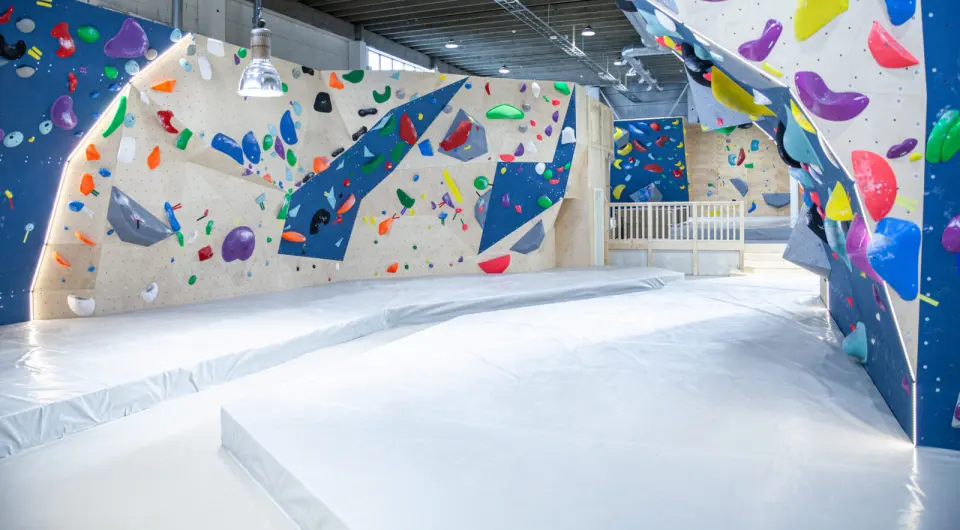 Long bouldering walls in blue and plywood above thick grey matting