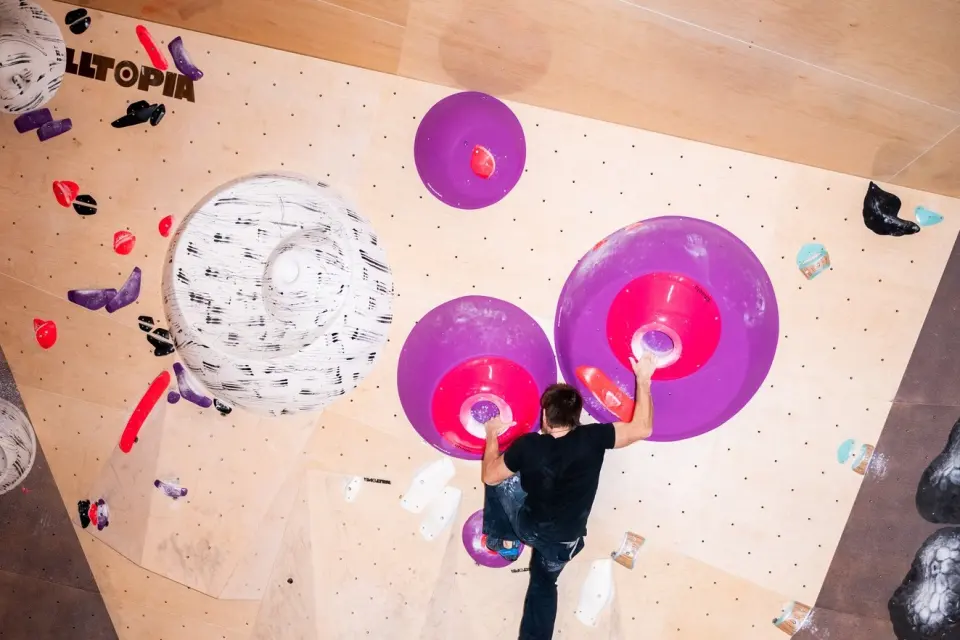 Climber seen from above on a plywood bouldering wall with large purple volumes