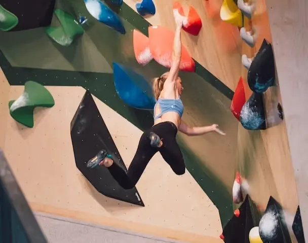 Climber reaching across a steep bouldering wall with coloured holds